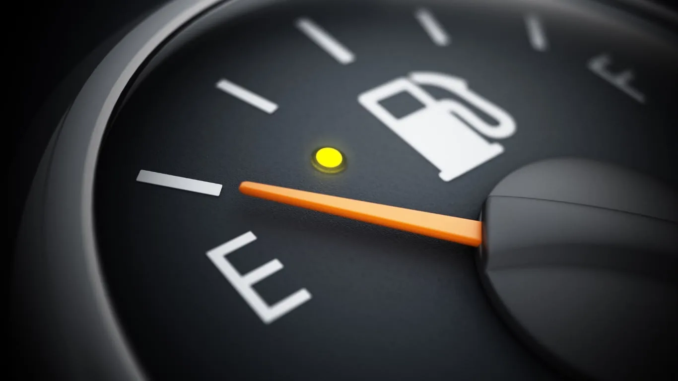 Close-up of a car fuel gauge showing the orange needle near empty and the yellow warning light on.