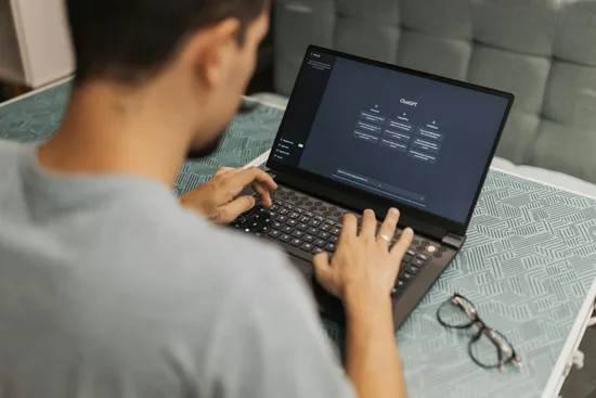 Person typing on a laptop displaying a dark software dashboard on screen.