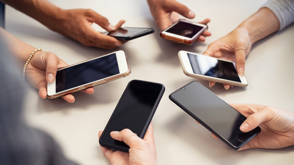 Group of people around a table, each holding a smartphone facing outward, screens off.